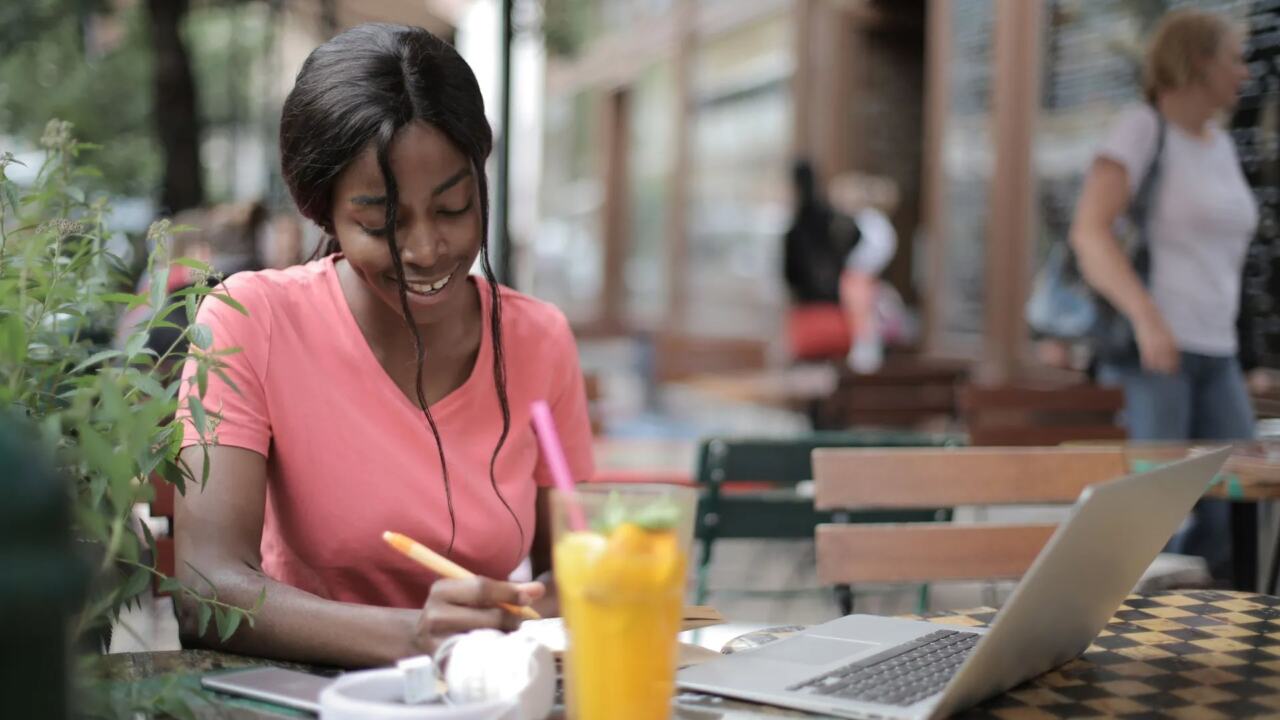 A young woman writing with headphones and music at a cafe